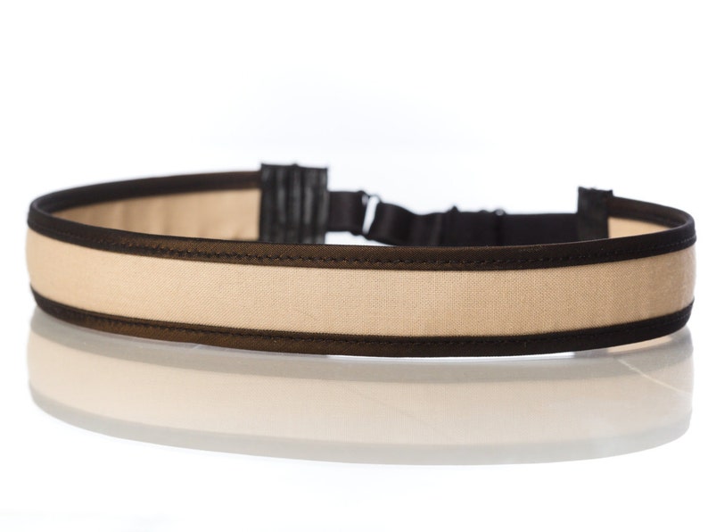 May include: A beige headband with black trim. The headband is made of a soft, comfortable fabric and has a subtle sheen.