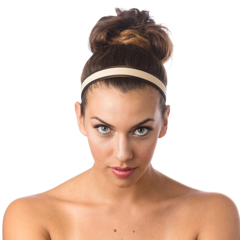May include: A woman with brown hair styled in a bun, wearing a beige headband with a black stripe. She is looking directly at the camera with a serious expression.