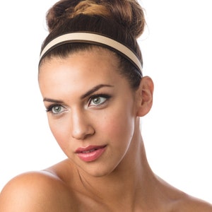 May include: A woman with brown hair styled in a bun wears a beige headband with a brown trim. She is looking off to the side with a neutral expression.