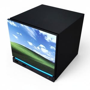 May include: A black cube-shaped computer tower featuring a front display panel showing a green grassy hill under a blue sky with white clouds. The base of the unit includes a horizontal blue light strip and a circular power button on the bottom right.