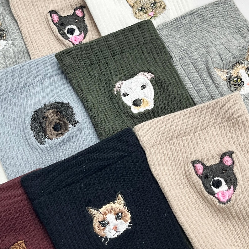 May include: Assortment of ribbed socks in various colors, each featuring an embroidered pet face. The collection includes socks in shades of black, green, beige, and gray, with dog and cat designs. The socks are a cozy and stylish accessory.