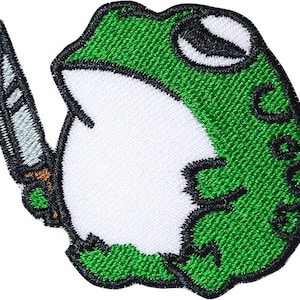 May include: Embroidered patch featuring a green frog holding a knife. The frog has a white belly, black eyes, and a black outline. The knife has a silver blade and a brown handle. The word "Cabbage" is written on the frog.
