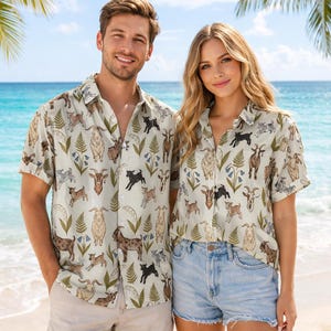 Könnte beinhalten: Zwei Personen tragen passende kurzärmlige Button-Down-Hemden mit einem Ziegenmuster. Die Hemden sind hellbeige mit Illustrationen von Ziegen, grünen Farnen und blauen Blumen. Sie stehen an einem Sandstrand.