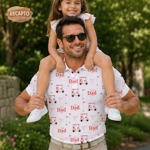 Op de afbeelding: Witte poloshirt met een golfkarretje en vlaggenpatroon, met het woord "Dad" erop gedrukt. Een man met een zonnebril heeft een kind op zijn schouders. Het shirt is een cadeau met een golfthema.