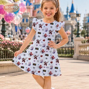 May include: A white dress with a pattern of Spider-Man characters, hearts, and spiderwebs. The dress has short sleeves with ruffled edges and a fitted waist. The girl is smiling and standing in front of a castle.