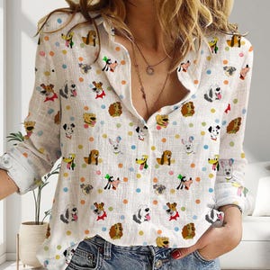 May include: White button-down shirt with a repeating pattern of cartoon dog illustrations and colorful polka dots. The long-sleeved shirt has a classic collar and buttoned cuffs. The dog illustrations feature various breeds and styles.