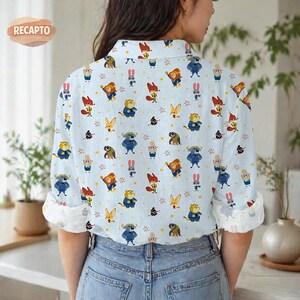 May include: Light blue button-down shirt with a repeating pattern of cartoon animals, including foxes, rabbits, and bears. The shirt has rolled-up sleeves with a white patterned lining. The Recapto logo is visible in the upper left corner.
