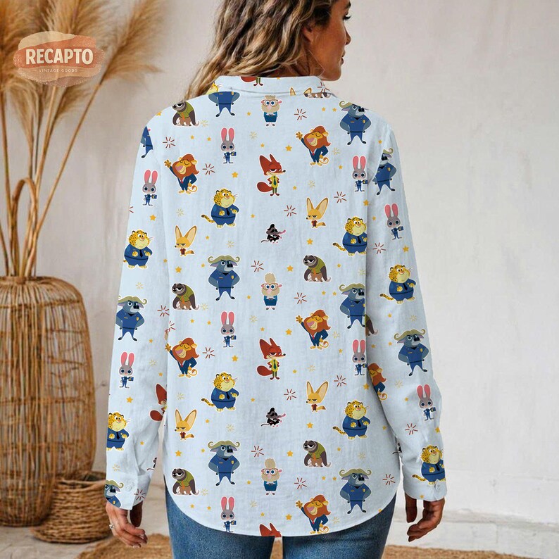 May include: Light blue button-down shirt with a repeating pattern of cartoon animal characters. The long-sleeved shirt features illustrations of foxes, rabbits, tigers, and other creatures in various poses, with yellow stars scattered throughout.