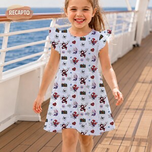 May include: A white dress with a pattern of Spider-Man figures, hearts, and spiderwebs. The dress has short, ruffled sleeves and a round neckline. The dress is knee-length and appears to be made of a lightweight fabric.