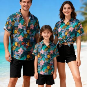 Könnte beinhalten: Passende hawaiianische Familienhemden mit Stitch-Cartoon-Charakter, tropischen Blumen und Blättern in Blau, Rosa und Gelb auf dunkelblauem Grund. Die Hemden werden mit schwarzen Shorts kombiniert, was einen koordinierten Familienlook ergibt.