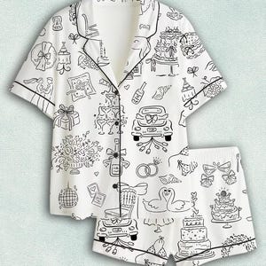 May include: A white short-sleeved pajama set with black piping and a repeating line-art pattern featuring wedding-themed illustrations including a tiered cake, a car with ribbons, champagne glasses, two swans, rings, and floral bouquets.