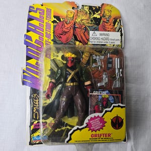 May include: A packaged action figure of "Grifter" from the WildC.A.T.S. comic series. The figure is in a clear plastic case with a yellow and purple card backing. The figure is wearing a green coat, brown pants, and a red mask. Includes a special edition collector card.