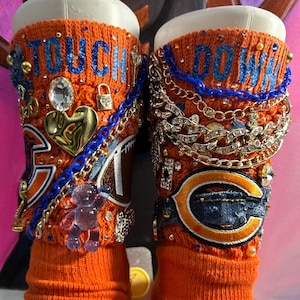 May include: Pair of orange socks with the words "TOUCH DOWN" in blue. The socks are embellished with gold chains, rhinestones, and a clear teddy bear charm. A Chicago Bears logo patch is also visible.