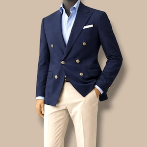 Può includere: Un blazer blu navy a doppio petto con bottoni dorati, abbinato a una camicia azzurra e pantaloni color crema. L'outfit è esposto su un manichino. Il testo "GOODCHOICEBySameer" è visibile in alto.