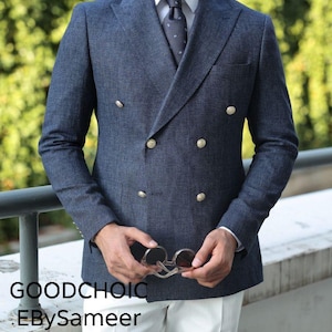 Może przedstawiać: Granatowa dwurzędowa marynarka z złotymi guzikami, w połączeniu z białą koszulą, wzorzystym krawatem i białymi spodniami. Marynarka ma teksturowaną tkaninę. Okulary przeciwsłoneczne trzymane są w dłoniach. Widoczny jest tekst "GOODCHOIC" i "EBySameer".