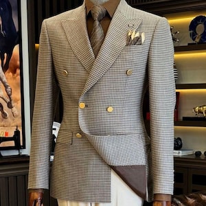 Może przedstawiać: Dwurzędowy garnitur w brązowo-białą kratę pepitkę, ze złotymi guzikami, pasującym krawatem i poszetką. Garnitur jest zestawiony z kremowymi spodniami. U góry widoczny jest napis "GOODCHOICEBySameer".