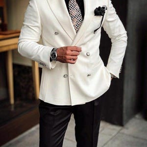 May include: A double-breasted ivory suit with black trousers. The suit features a patterned tie, a black pocket square, and a wristwatch. The text "GOODCHOICEBySameer" is visible at the top of the image.