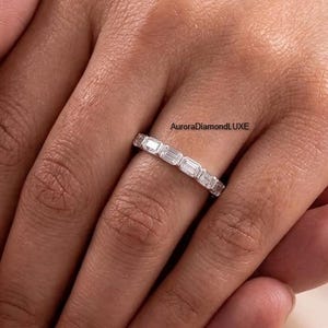 May include: A silver ring with multiple rectangular-cut gemstones. The ring is on a person's finger, with another person's hand gently holding the hand with the ring. The ring is from AuroraDiamondLuxe.