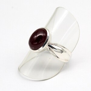 May include: A silver ring featuring a polished, oval-shaped deep red gemstone set in a smooth metal bezel. The band is crafted from a reflective silver-toned metal with a tapered design that widens slightly as it reaches the central stone setting.