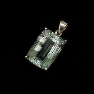 Pode incluir: Pingente retangular de pedra preciosa verde claro com argola de prata. A pedra preciosa é facetada, refletindo a luz. O pingente está em um fundo preto.
