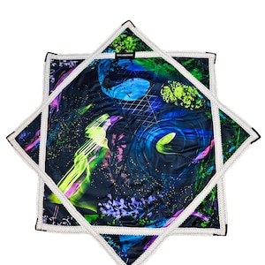 May include: A star-shaped quilted fabric piece featuring a dark blue background with vibrant neon green, purple, and blue abstract patterns, including grid lines and swirling shapes. The edges are finished with a white zigzag stitched border.