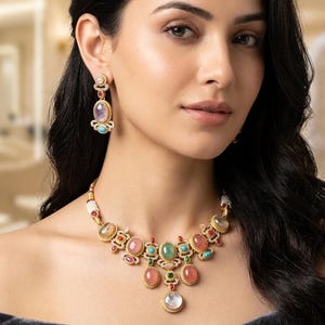 May include: A gold necklace and earring set with a variety of colourful gemstones. The necklace features oval and round stones in pink, green, and blue hues. The earrings have a similar design, with a large oval stone and smaller accent stones.