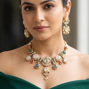May include: A gold-toned necklace and matching earrings set. The necklace features a central pendant with a large, clear stone, surrounded by smaller stones in various colors. The earrings have a similar design. The jewelry is set against a dark green dress.
