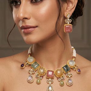 May include: A gold-toned statement necklace and matching drop earrings featuring an array of multi-colored gemstones including pink, green, and translucent stones. The jewelry is accented with small white pearls and clear pavé-set crystals.