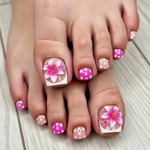 May include: A pedicure featuring a white base with bright pink polka dots on most toenails, while the big toes showcase a detailed pink and white lily flower design with a white French tip style border on a clear base.