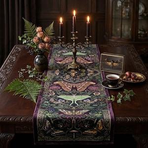 May include: A dark purple velvet table runner featuring a detailed botanical print of various moths, ferns, and flowers. The runner is centered on a wooden table with a brass candelabra, a vase of roses, a teacup, and a framed moth specimen.