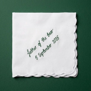 May include: A square white handkerchief with scalloped edges featuring dark green embroidered cursive text that reads "father of the bear" followed by the date "6 September 2026" positioned diagonally across the centre of the fabric.