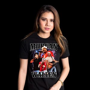 Pu&ograve; includere: T-shirt nero con grafica del cantante country Morgan Wallen. La grafica include un'immagine di Morgan Wallen e di altri membri della band, con il nome "MORGAN WALLEN" in bianco, in un font stilizzato. La maglietta &egrave; indossata da una persona.