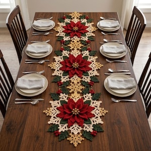 May include: A long, rectangular crochet table runner featuring three large, dimensional red poinsettia flowers, dark green leaves, and cream-colored snowflake patterns with small red berries, centered on a dark wood dining table with place settings.