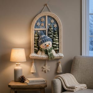 May include: A crocheted wall hanging shaped like an arched window featuring a snowman wearing a blue knit hat and green plaid scarf. The scene includes green pine trees, white snowflakes, and a blue background. Three cream tassels hang from the base.