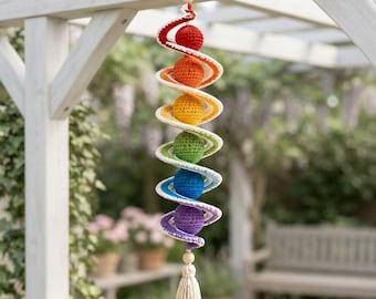 Puede incluir: Una decoración colgante en espiral con seis esferas de ganchillo en rojo, naranja, amarillo, verde, azul y morado. Las esferas están unidas por una estructura en espiral de ganchillo blanca, rematada con una cuenta de madera y una borla.