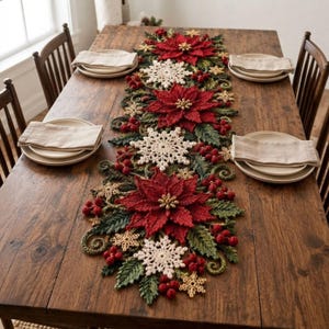 Può includere: Un lungo runner da tavola all'uncinetto con fiori di stella di Natale rossi, fiocchi di neve color crema, foglie verdi e piccole bacche rosse. Il runner è centrato su un tavolo da pranzo in legno con quattro coperti, piatti e tovaglioli.