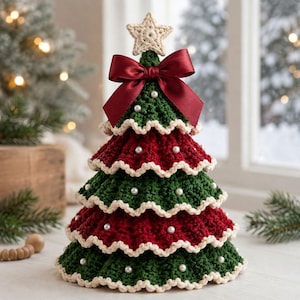 May include: A tiered crochet Christmas tree featuring alternating dark green and deep red layers with scalloped cream-coloured edges. The tree is decorated with small white pearl-like beads, topped with a cream crochet star, and finished with a large dark red satin bow.