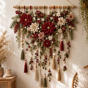 Peut inclure: Une décoration murale composée de fleurs de poinsettia crochetées rouges et blanches, de feuillage vert et de baies rouges sur une tige en bois. L'ensemble comprend des cordons suspendus ornés de perles en bois et de pompons rouges, beiges et verts.