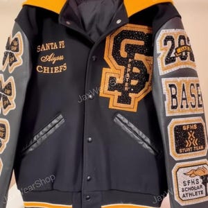 以下が含まれることがあります： 黒とゴールドのアクセントが施された黒色のスタジアムジャンパー。 「SANTA FE Alyssa Chiefs」と「PEPSTER」の文字と大きな「SF」ロゴが特徴です。「BASE」、「STUNT TEAM」、「SCHOLAR ATHLETE」と書かれたパッチが含まれています。
