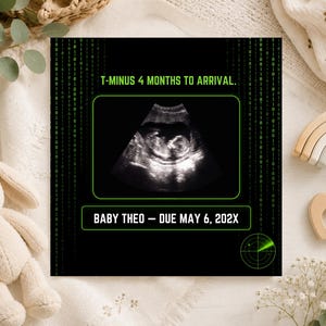 K&ouml;nnte beinhalten: Ein schwarzes, rechteckiges Schild zur Schwangerschaftsank&uuml;ndigung mit gr&uuml;nem Bin&auml;rcode-Hintergrund, einem zentralen Ultraschallbild und dem Text T-MINUS 4 MONTHS TO ARRIVAL und BABY THEO &ndash; DUE MAY 6, 202X, sowie einer gr&uuml;nen Radargrafik.