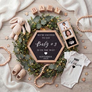May include: A hexagonal black felt letter board with white text reading WE'RE EXCITED TO SAY Baby #3 IS ON THE WAY! SEPTEMBER 202X, surrounded by a green eucalyptus wreath with fairy lights, a plush bunny, baby shoes, a onesie, and photos.
