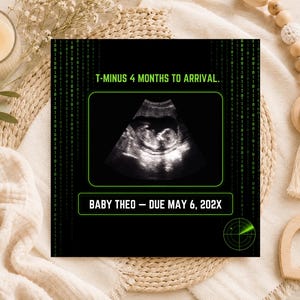 K&ouml;nnte beinhalten: Eine schwarze, rechteckige Ank&uuml;ndigungskarte mit gr&uuml;nem digitalen Matrix-Hintergrund, einem zentralen Ultraschallbild und dem Text T-MINUS 4 MONTHS TO ARRIVAL sowie BABY THEO &ndash; DUE MAY 6, 202X, mit einer kleinen gr&uuml;nen Radargrafik in der Ecke.