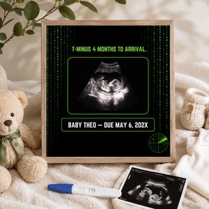 K&ouml;nnte beinhalten: Ein gerahmter Digitaldruck mit schwarzem Hintergrund, gr&uuml;nem Bin&auml;rcode, einem zentralen Ultraschallbild und dem Text T-MINUS 4 MONTHS TO ARRIVAL sowie BABY THEO &ndash; DUE MAY 6, 202X, mit einer Radargrafik in der unteren rechten Ecke.