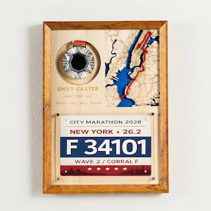 May include: Wooden framed artwork featuring a marathon medal and a map of New York City. The artwork includes the text "EMILY CARTER" and "CITY MARATHON 2026 NEW YORK 26.2". The frame is a warm brown color.
