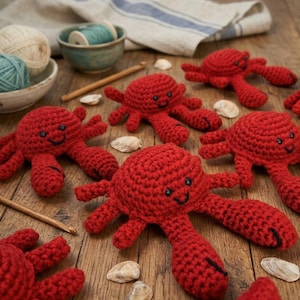 Puede incluir: Una colección de cangrejos rojos de ganchillo hechos a mano, con caras sonrientes y detalles negros. Los cangrejos están dispuestos sobre una superficie de madera con conchas marinas, hilo y ganchos de ganchillo, sugiriendo un tema náutico o de playa.