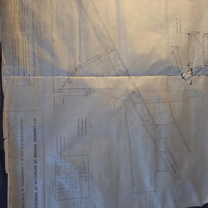 Peut inclure: Plan ancien d'un dispositif mécanique, probablement pour la réparation de parachutes, avec des dessins au trait détaillés et du texte. Le papier est vieilli, montrant des plis et de l'usure. Un mètre ruban jaune est posé en bas.