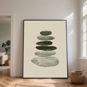 May include: A framed art print featuring a stack of abstract, oval-shaped stones in varying shades of green and gray. The artwork is set against a cream-colored background, creating a minimalist and modern aesthetic. The print is displayed in a black frame.