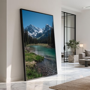 Puede incluir: Una impresión enmarcada de un paisaje montañoso con picos nevados, un lago turquesa y árboles de hoja perenne bajo un cielo azul claro. La impresión se exhibe en un entorno interior moderno.