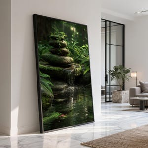 Puede incluir: Una impresión artística enmarcada que representa una serena escena de jardín zen. La obra presenta una pequeña cascada que cae en un estanque, con piedras apiladas y exuberante follaje verde. El marco negro realza la tranquilidad.
