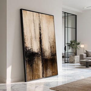 Op de afbeelding: Grote ingelijste abstracte kunstafdruk. Het kunstwerk toont verticale penseelstreken in tinten beige, bruin en zwart. Het zwarte frame complementeert het kunstwerk en creëert een moderne esthetiek. De print leunt tegen een witte muur in een goed verlichte kamer.